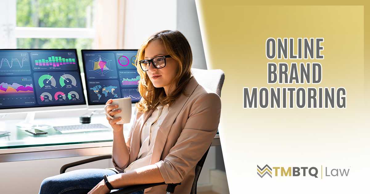 Woman in blazer and glasses sitting at a desk holding a coffee mug, with two large monitors behind her displaying colorful business analytics dashboards showing charts, graphs, and KPIs.