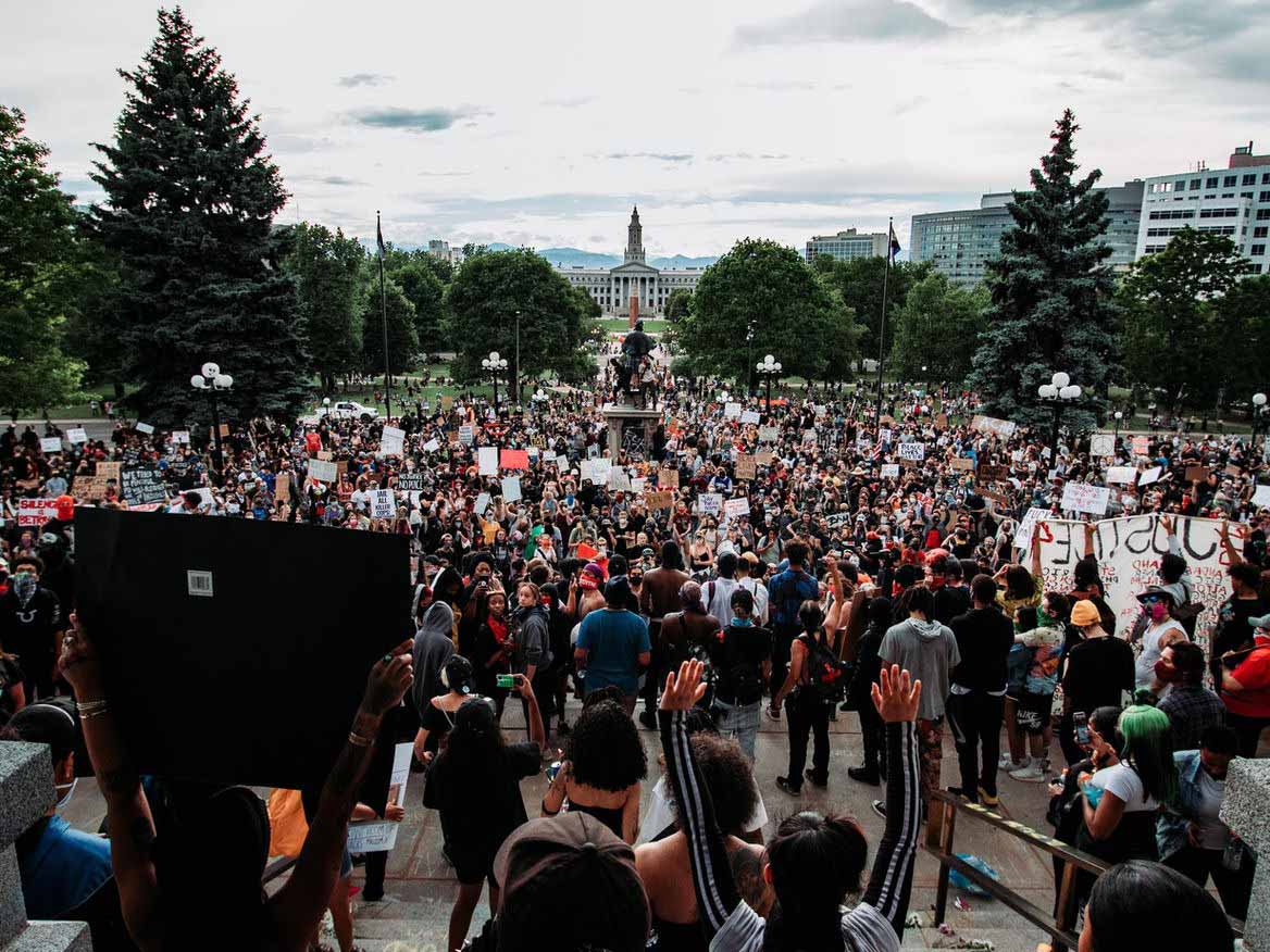 Large crowd of protesters gathered on the lawn in front of a state capitol building