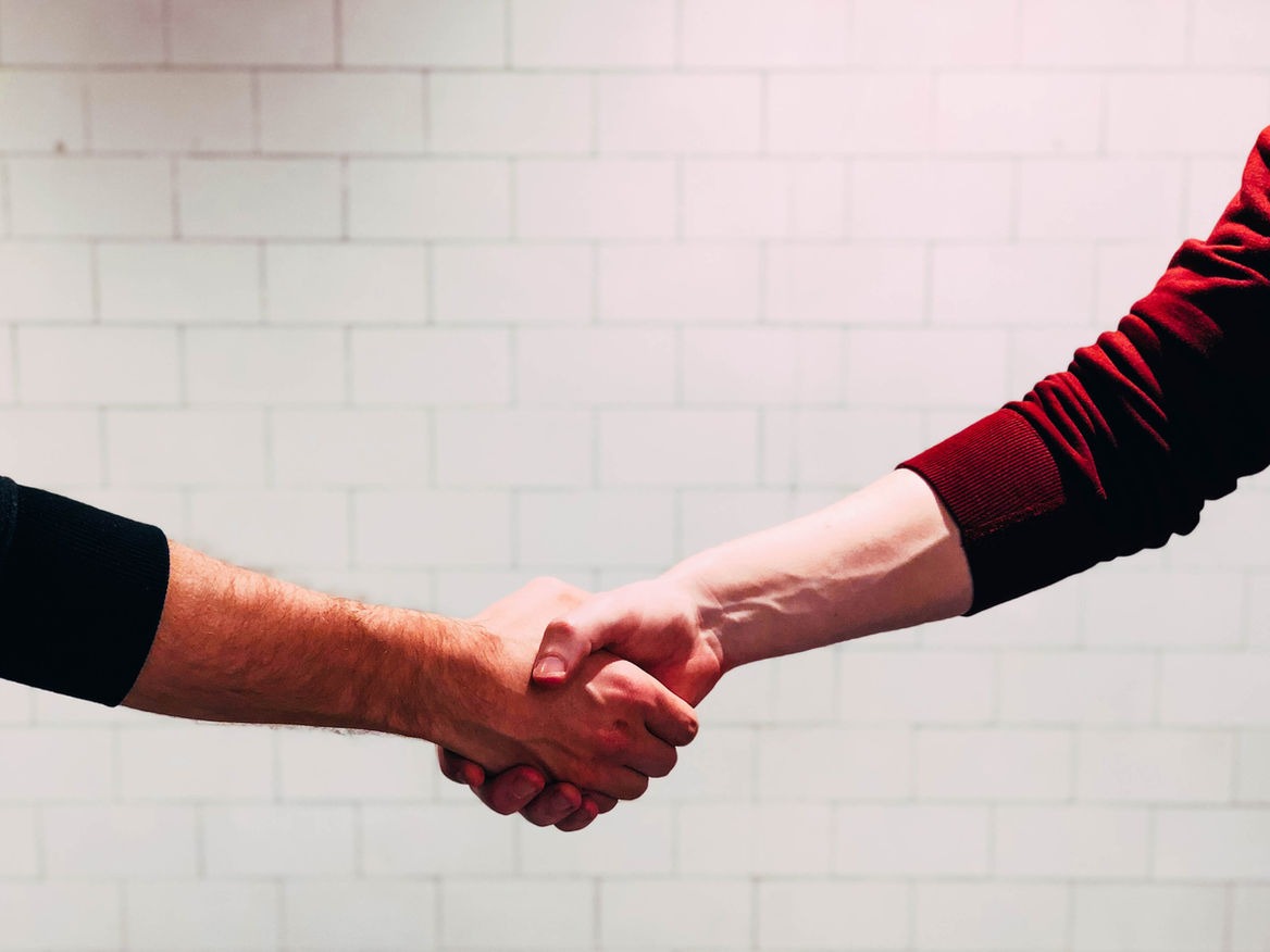 Two people shaking hands in front of a white brick wall