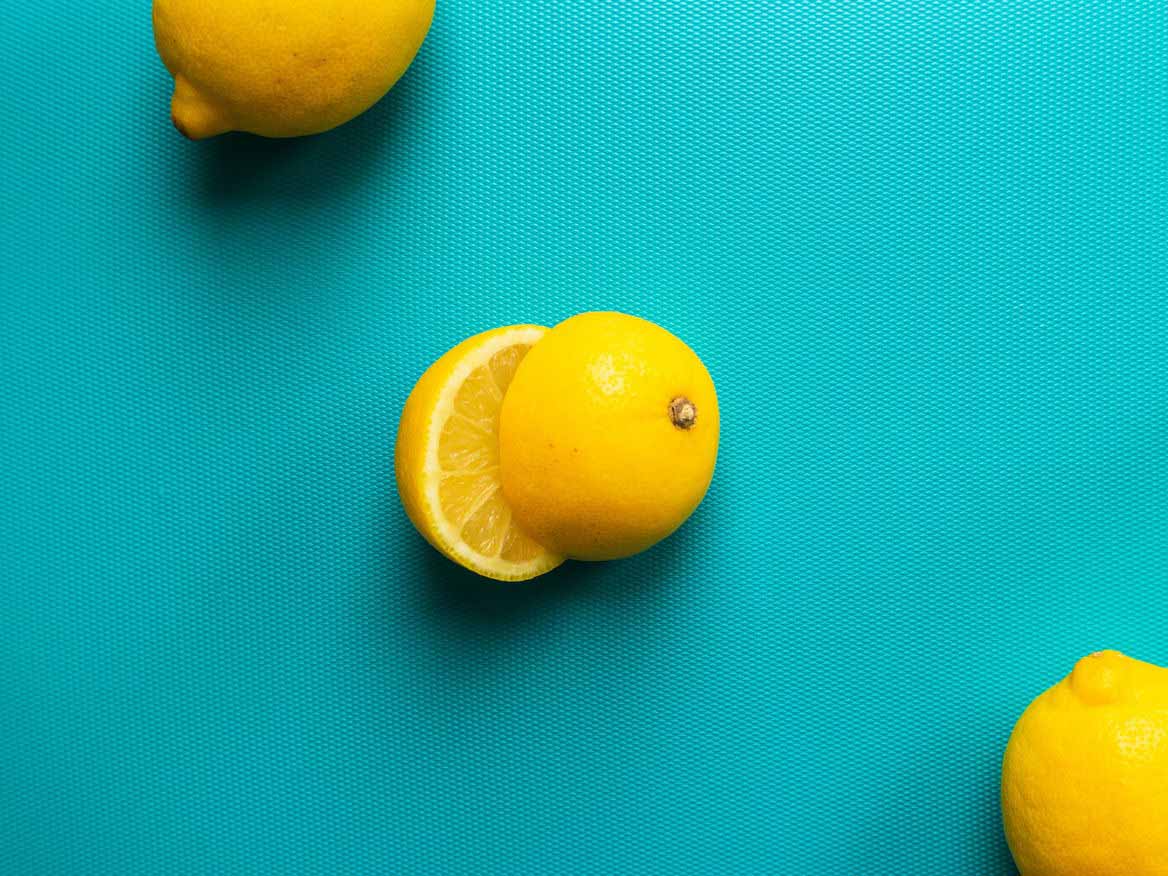 Whole and halved lemons on a bright turquoise background