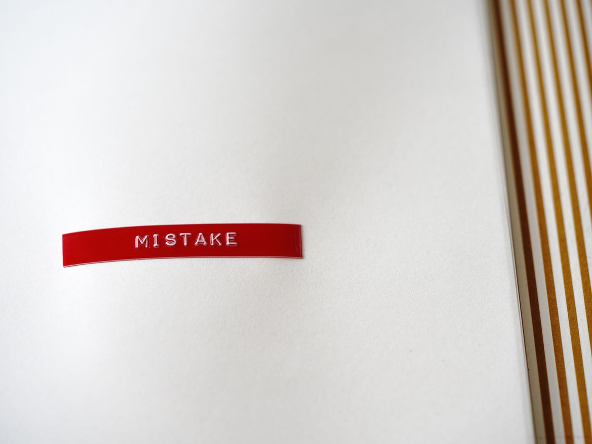 Red embossed label tape reading MISTAKE on a sheet of white paper