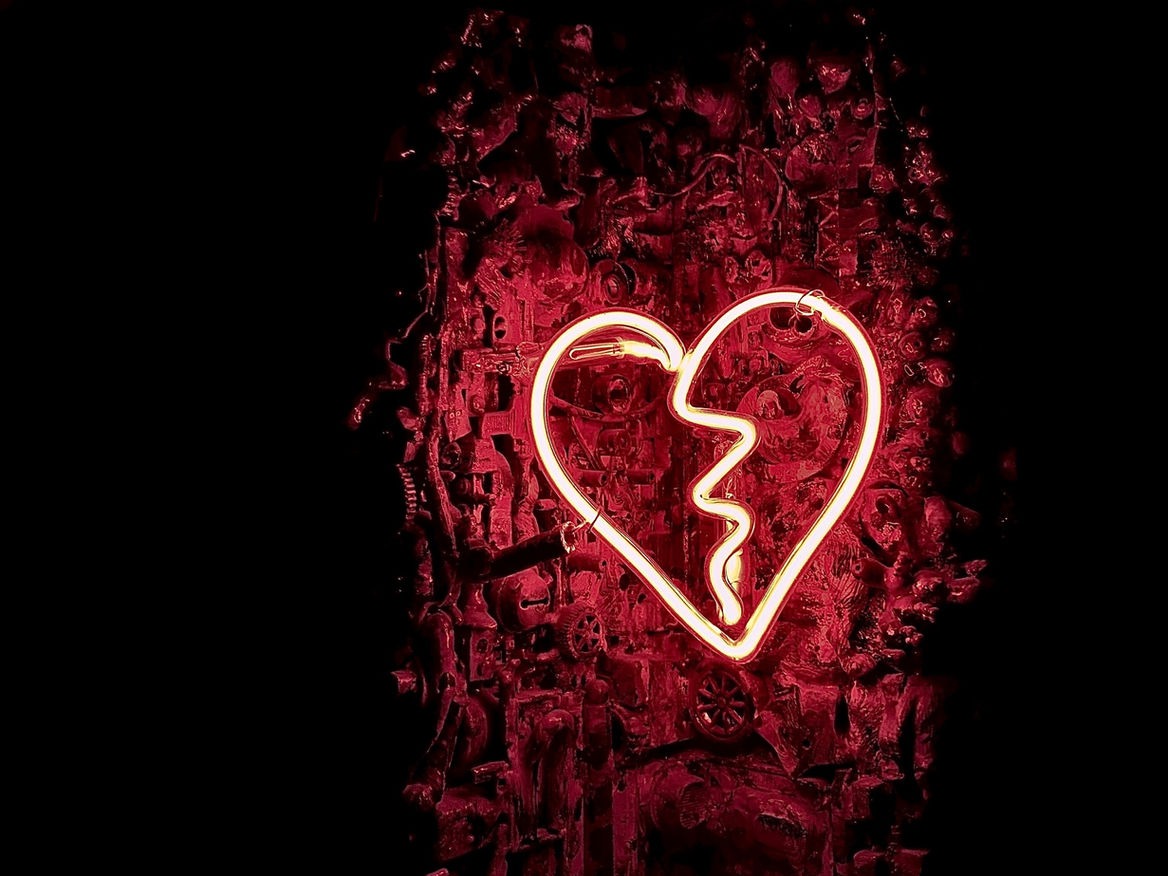 Red neon broken-heart sign glowing on a dark wall