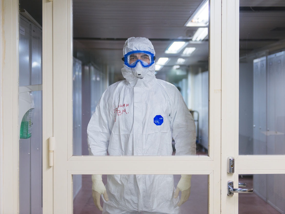 Person in a white hazmat suit, goggles and mask standing in a lab doorway