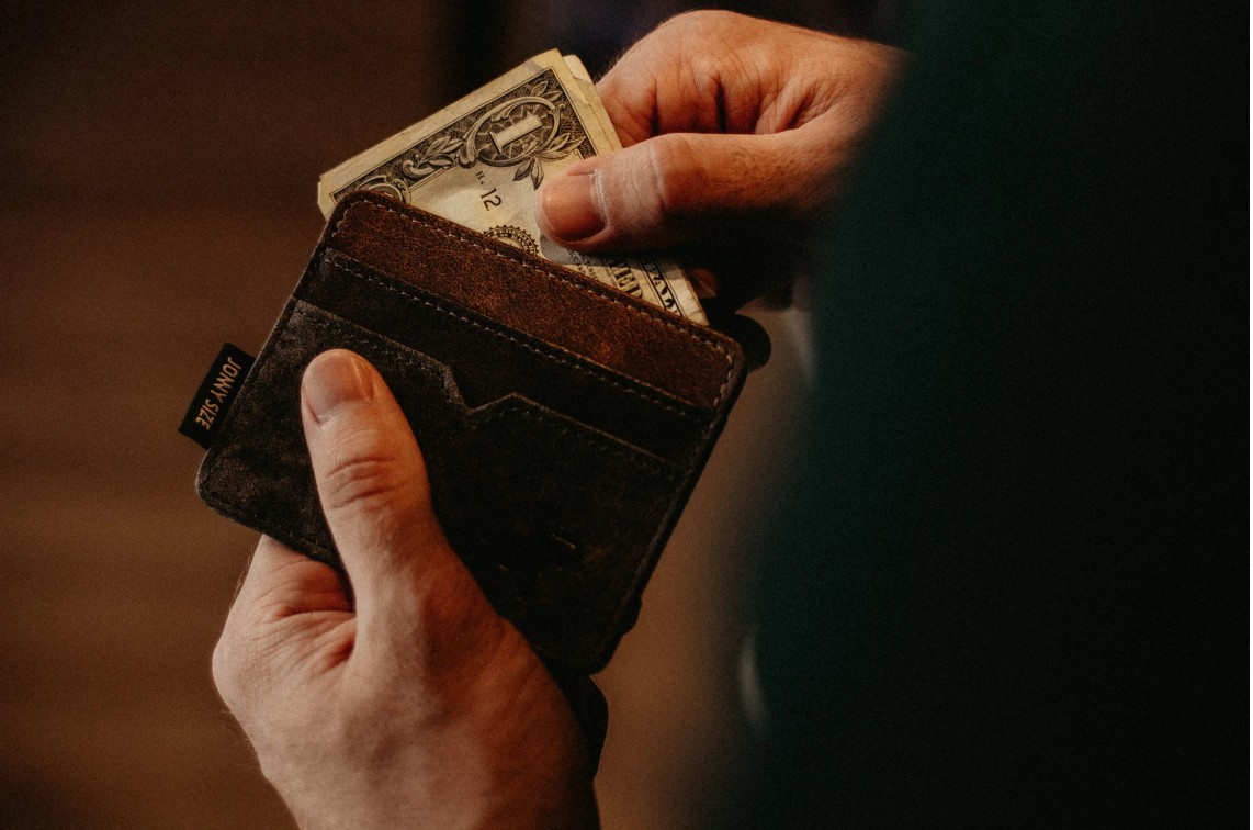Hand pulling dollar bills out of a worn leather wallet