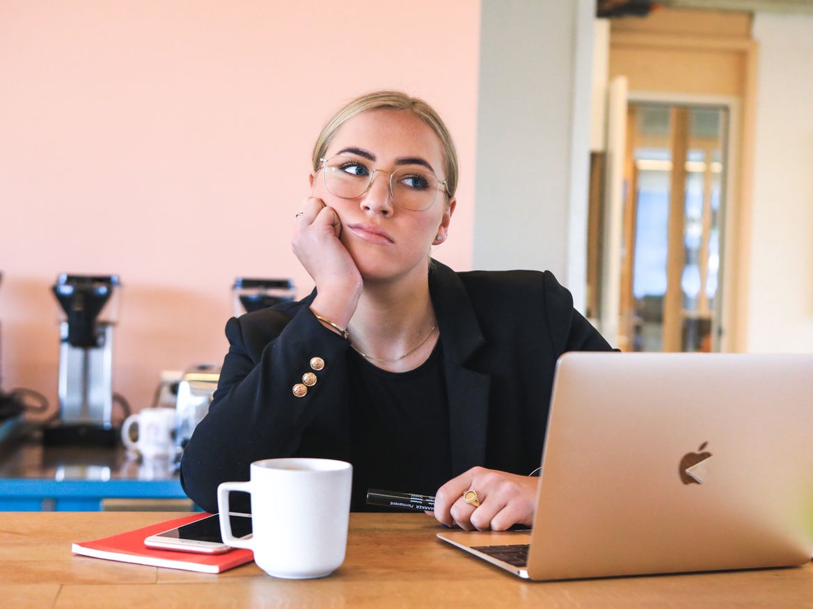 Skeptical woman in a blazer resting her chin on her hand at a laptop