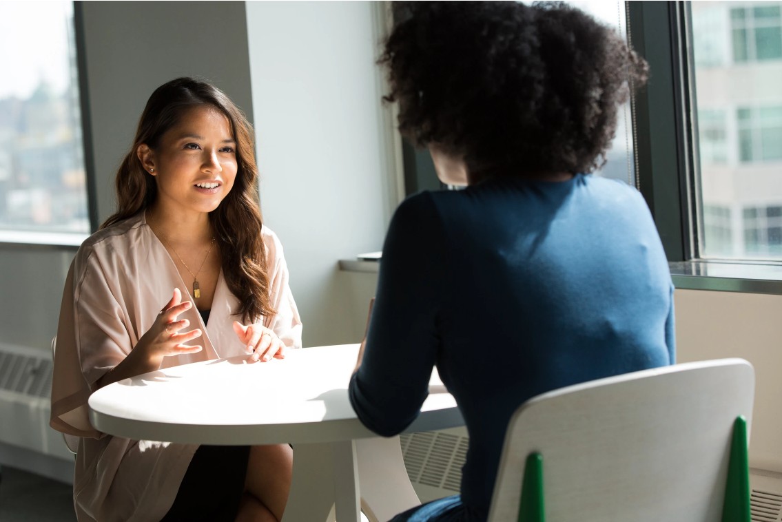 Two women talking across a small white table in a bright office