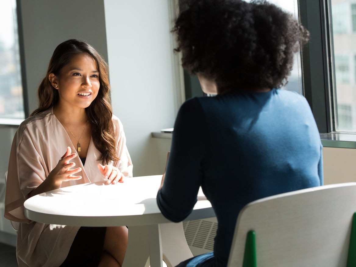 Two women talking across a small white table in a bright office